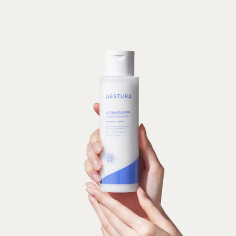 Hand holding a bottle of Aestura skincare product against a light background
