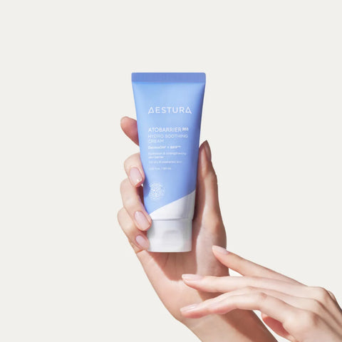 Hand holding a blue Aestura skincare tube against a light background