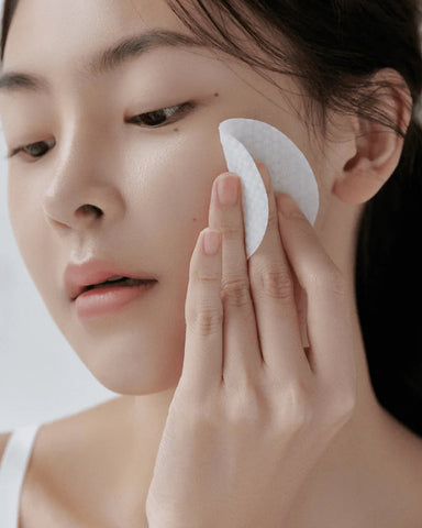 Person using a white cotton pad on their face against a neutral background