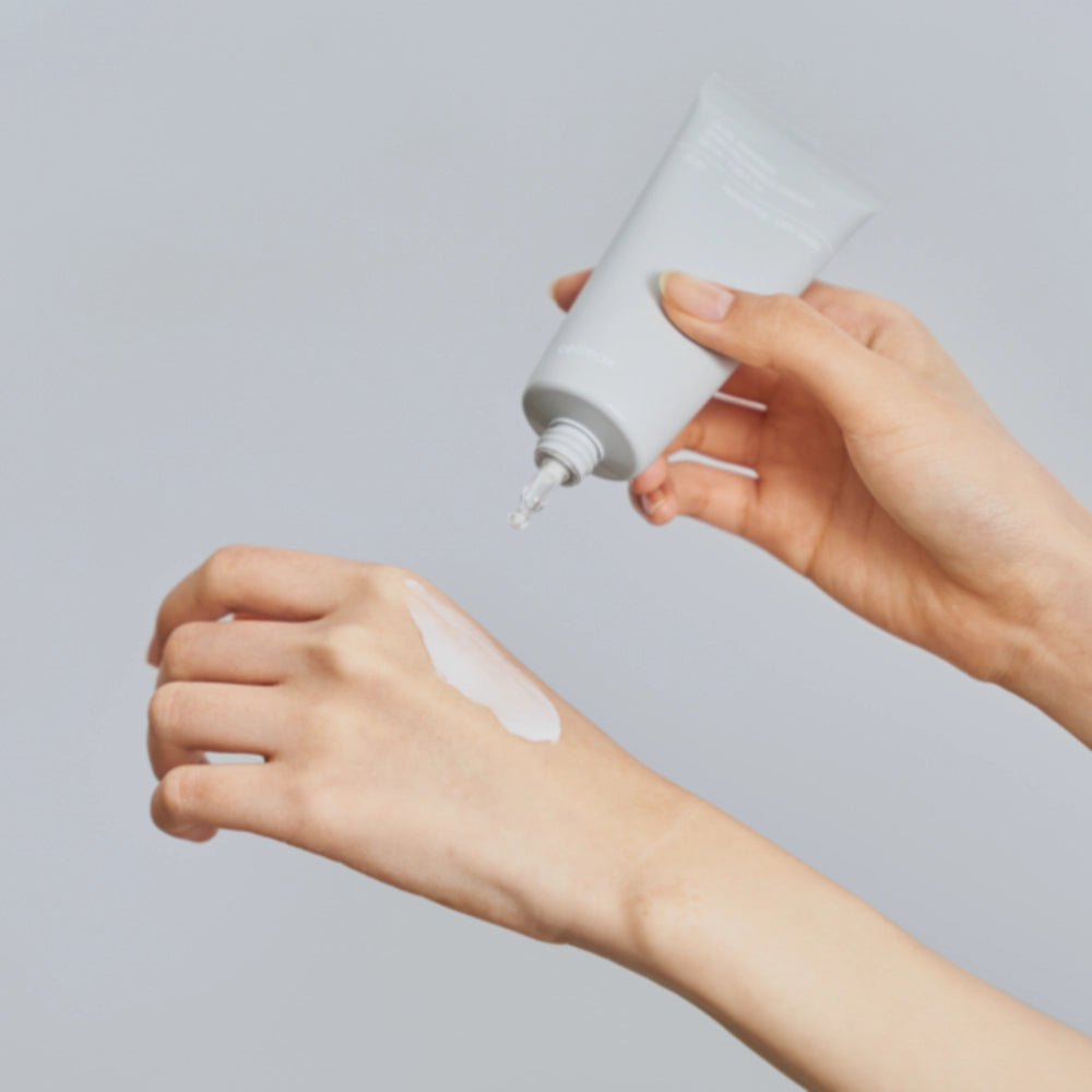 Person applying a white cream to their hand with a gray background