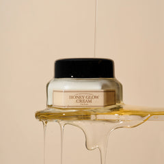 Jar of honey glow cream with honey flowing out on a beige background
