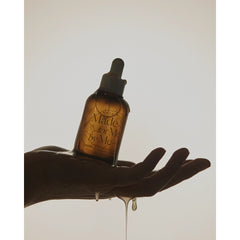 Amber glass bottle with dropper labeled 'Made for Me by Me' held in a hand with oil dripping.