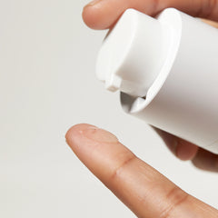 Hand applying a white cream to a finger against a light gray background