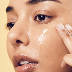 Close-up of a person applying cream to their face with a neutral background