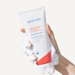 Hand holding a tube of Aestura Theracne Clean Cleanser on a white background