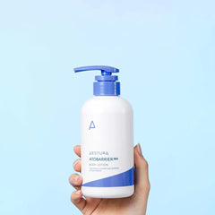 Hand holding a skincare product bottle with a blue and white design against a light blue background