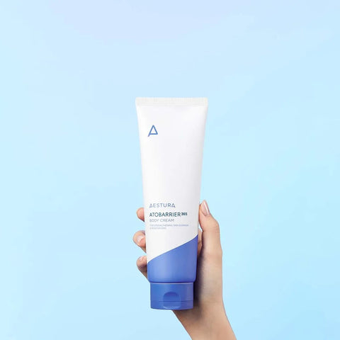 Hand holding a tube of Kiehl's cream against a light blue background