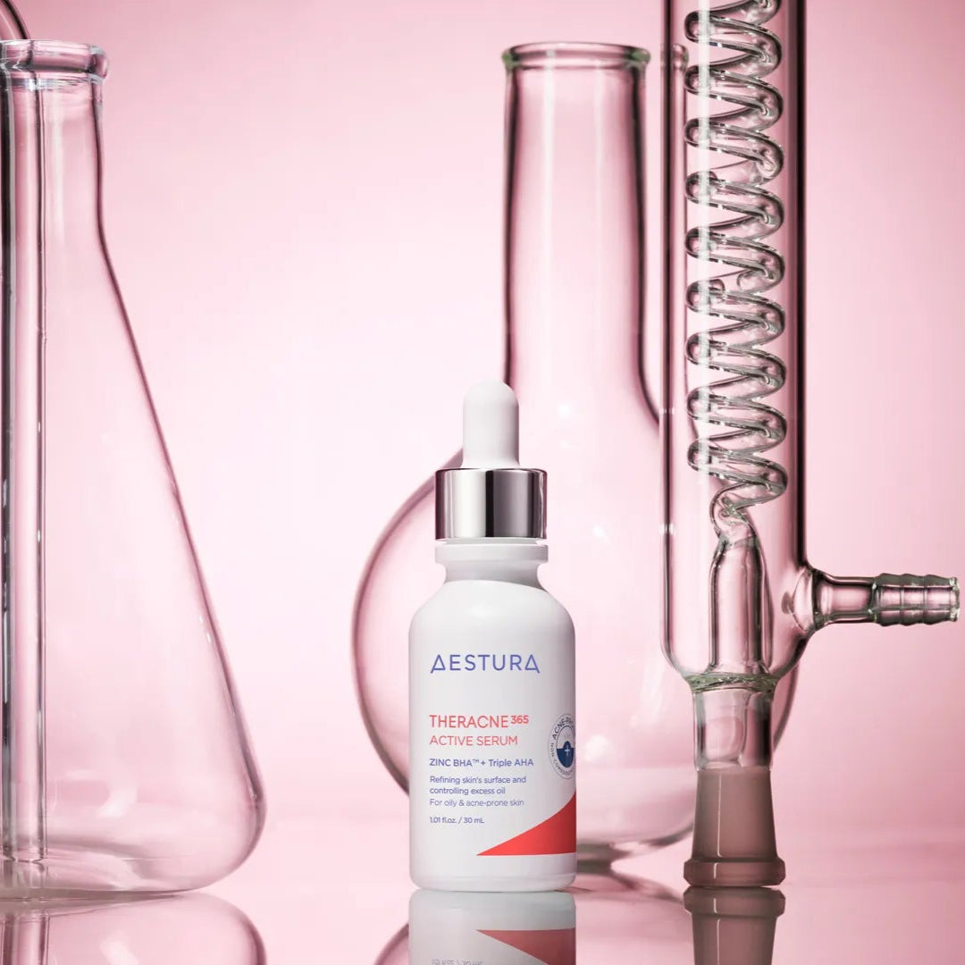 Skincare serum bottle labeled 'Aestura' with laboratory glassware on a pink background