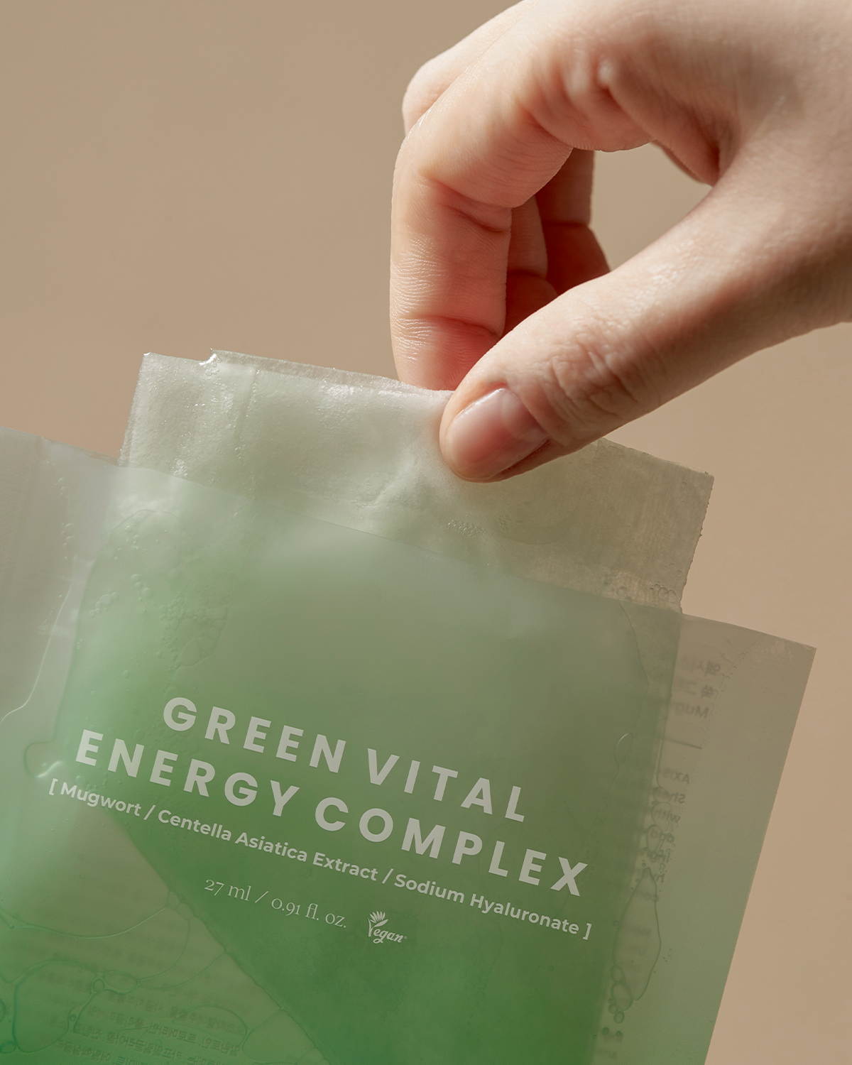 Hand holding a green packet labeled 'Green Vital Energy Complex' against a beige background