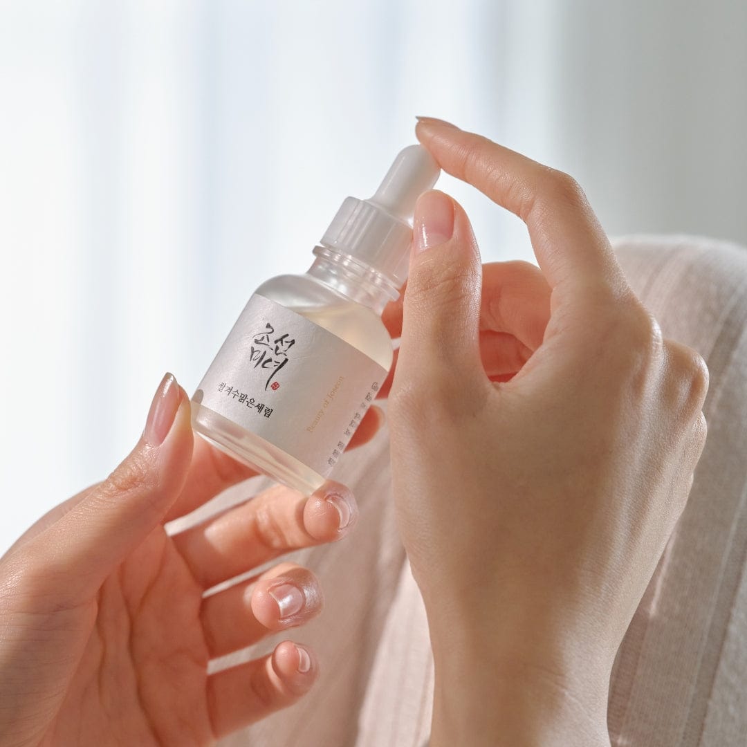 Hand holding a small skincare bottle with a dropper against a blurred background