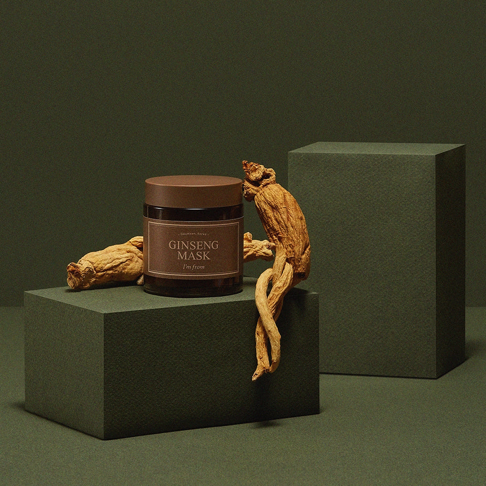 Jar of Ginseng Mask on a green platform with ginseng roots against a dark green background
