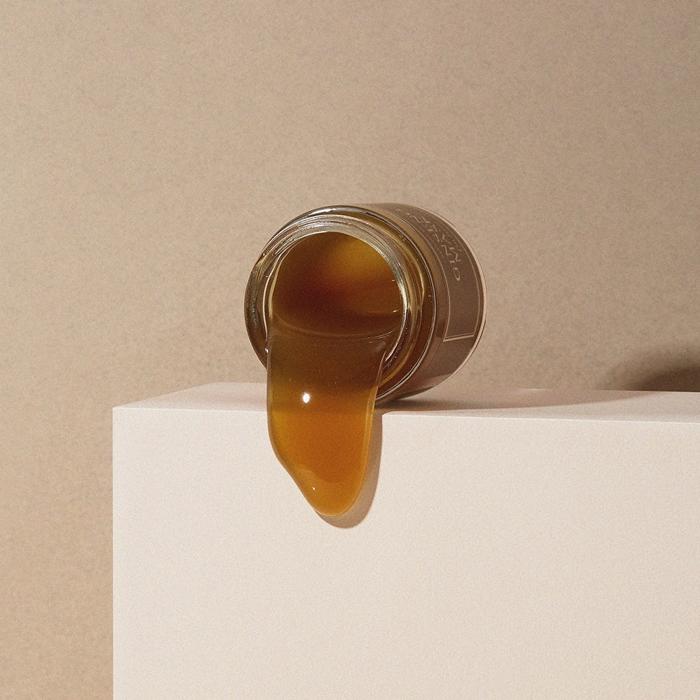 Jar of honey with honey dripping onto a beige surface