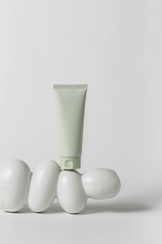 Green tube of cream on white eggs against a light gray background
