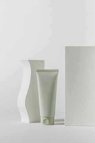Green skincare tube and white container on a light gray background