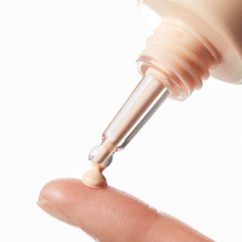 Close-up of a cosmetic dropper with a small amount of cream on a finger against a white background
