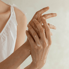 Person applying a moisturizing cream to their hands with a neutral background