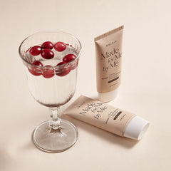 Two tubes of 'Made for Me' skincare product next to a glass with red berries on a beige background