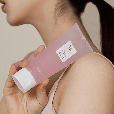 Person holding a pink skincare product with a white cap on a neutral background