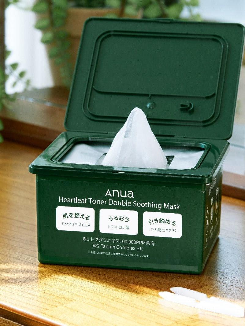 Green container of Anua Heartleaf Toner Double Soothing Mask on a wooden surface with plants in the background.
