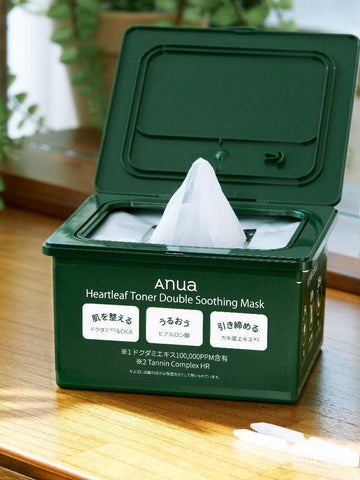 Green container of Anua Heartleaf Toner Double Soothing Mask on a wooden surface with plants in the background.