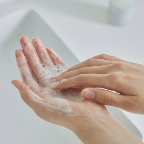 Hands with soap bubbles being washed against a blurred background