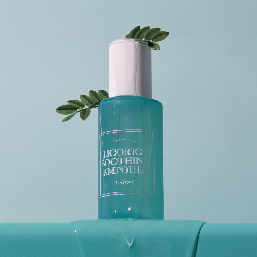 Skincare ampoule bottle with green leaves on a light blue background