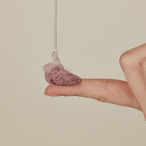 Hand holding a pink stone with a clear bead on a beige background