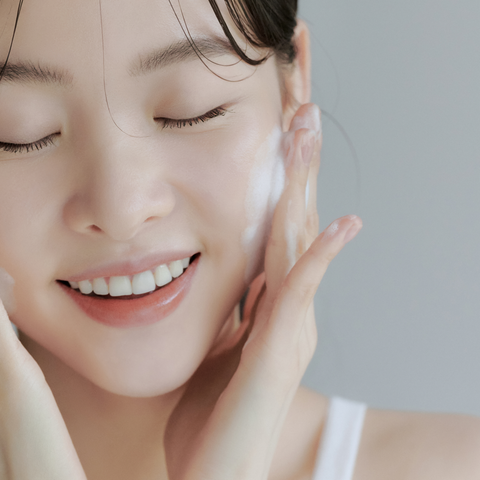 Woman applying cream to her face with a neutral background