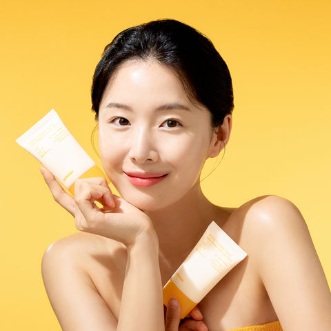 Woman holding skincare products against a yellow background