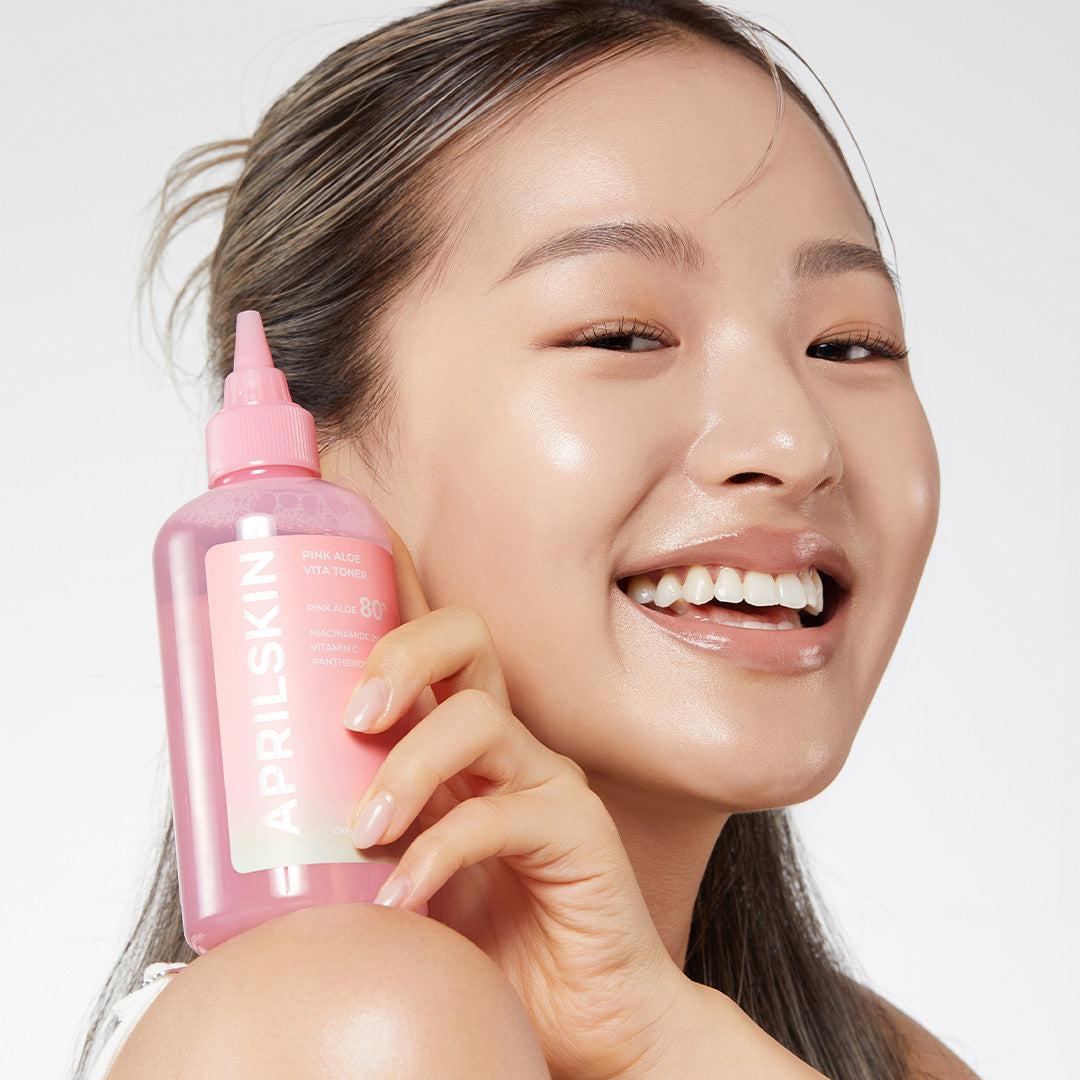 Woman holding a pink skincare bottle with a blurred background