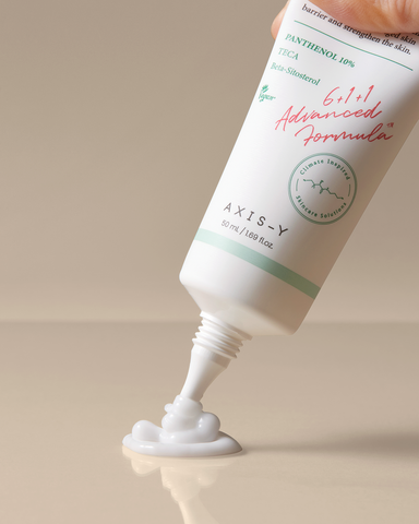 Tube of AXIS-Y skincare product with cream being squeezed out on a beige background