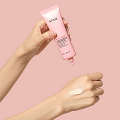 Hand holding a pink Anua product with a swatch on a pink background