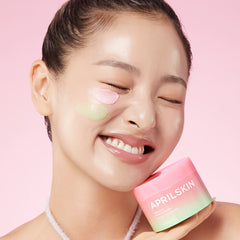 Woman holding a pink and green skincare product with 'APRILSKIN' branding against a pink background