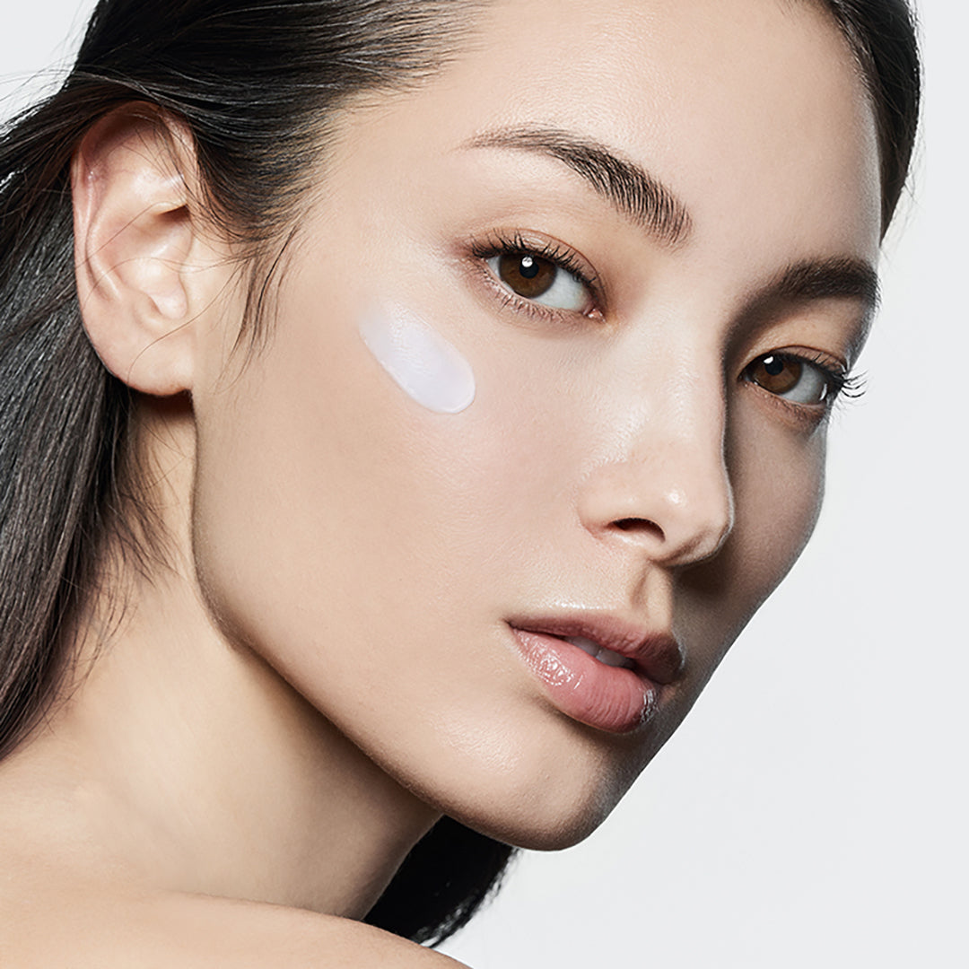 Close-up of a woman's face with a white patch on her cheek against a light gray background