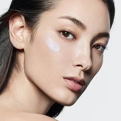 Close-up of a woman's face with a white patch on her cheek against a light gray background