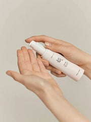 Person holding a white spray bottle with a beige background