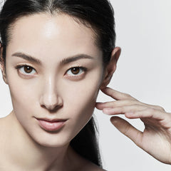 Close-up of a woman's face with a hand touching her hair against a light background