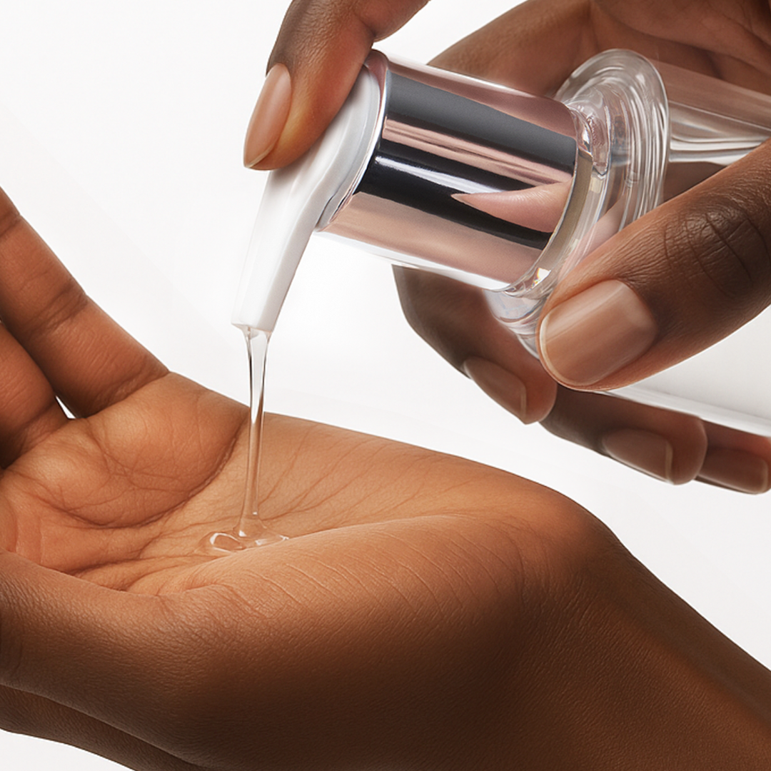 Clear liquid being poured from a bottle into a hand on a white background