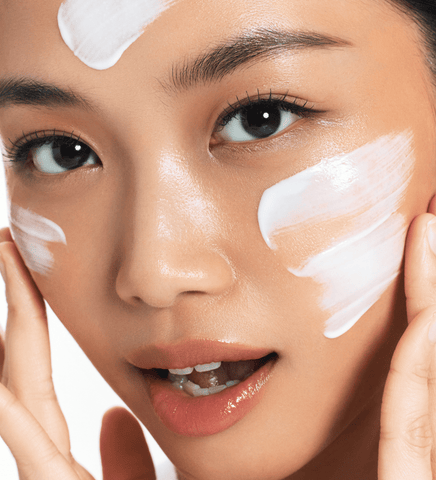 Close-up of a person applying cream to their face with a neutral background