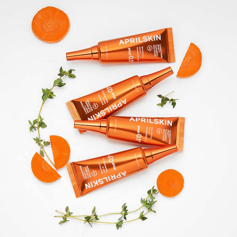 Four orange skincare bottles with 'APRILSKIN' branding on a white background with carrot slices and green leaves.