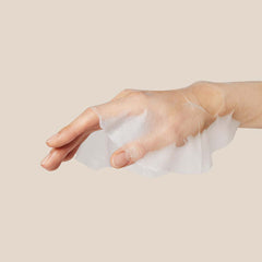 Hand holding a white cotton pad against a beige background