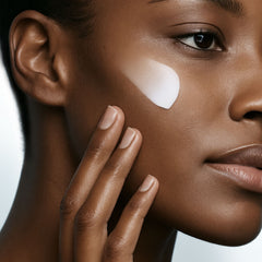 Close-up of a woman's face with a white patch on her cheek, against a neutral background