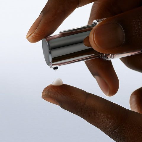 Hand holding a silver cylindrical object with a white cap against a light gray background