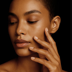 Close-up of a woman's face with one hand gently touching her cheek against a dark background
