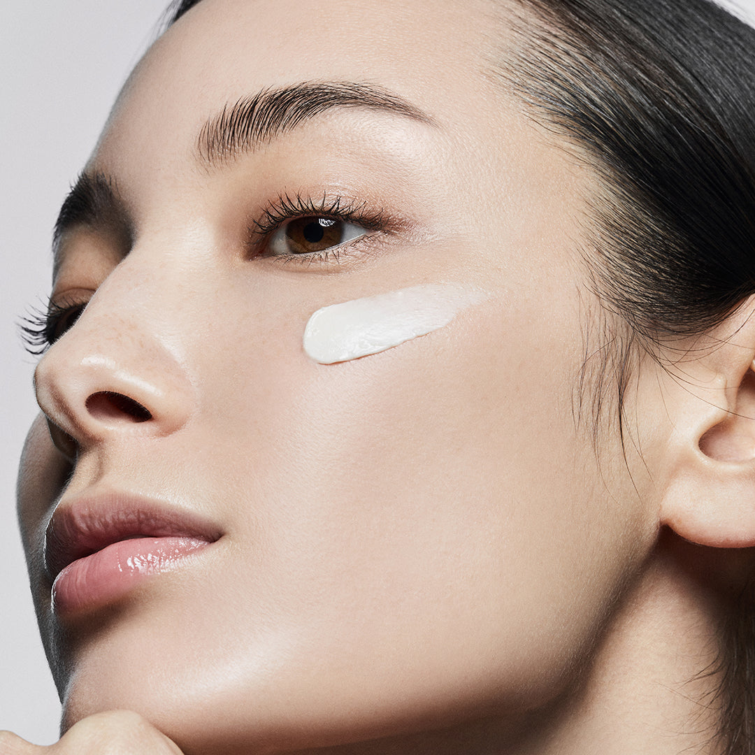 Close-up of a woman's face with a light product applied to her cheek against a neutral background