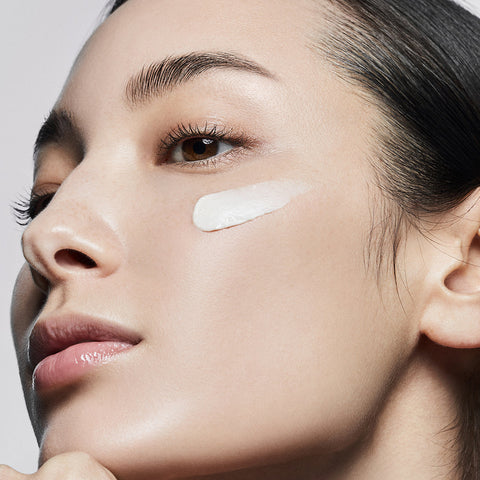 Close-up of a woman's face with a light product applied to her cheek against a neutral background