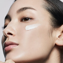 Close-up of a woman's face with a light product applied to her cheek against a neutral background