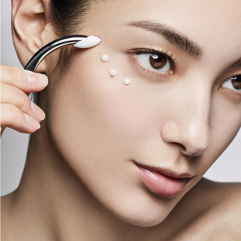 Close-up of a woman applying cream to her face with a small applicator.