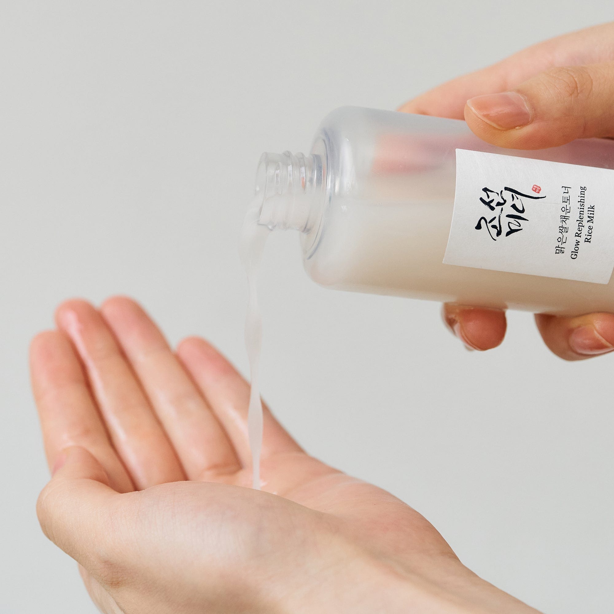 Hand holding a small container of rice milk with a white label against a light gray background
