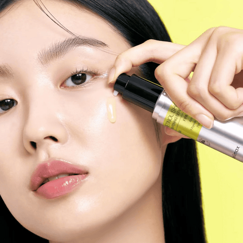 Person applying a cosmetic product to their face with a yellow background